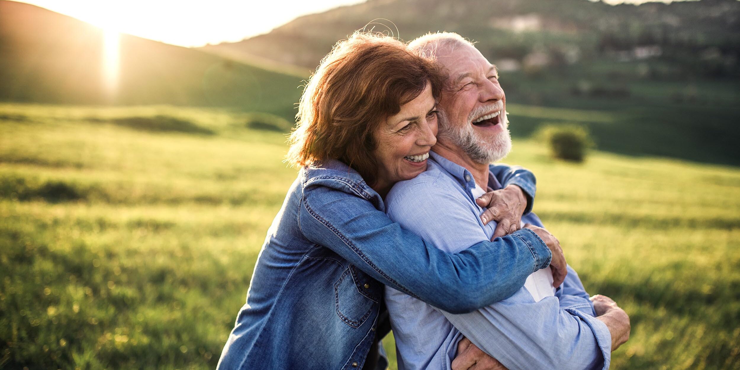 Side view of senior couple hugging outside in spring nature at sunset after their oral surgery