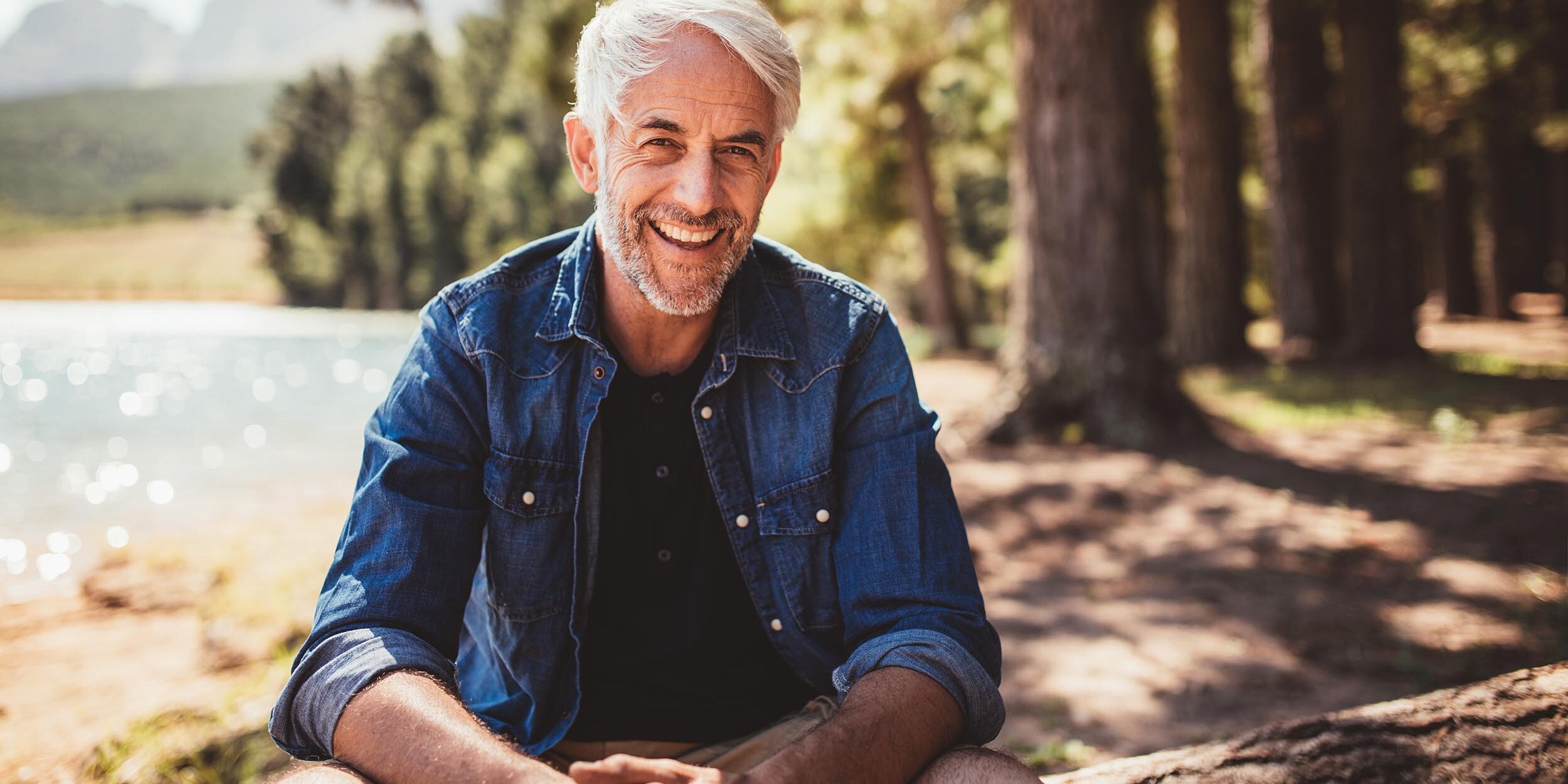 Happy mature man sitting near a lake after his dental bridge appointment